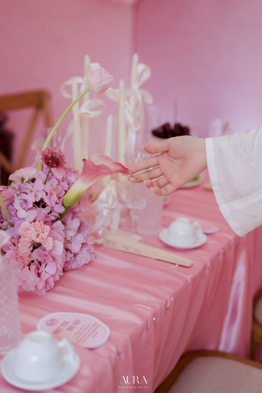 Cận cảnh cẩm tú cầu tím hồng, hoa rum và nến nơ trắng trên khăn satin hồng