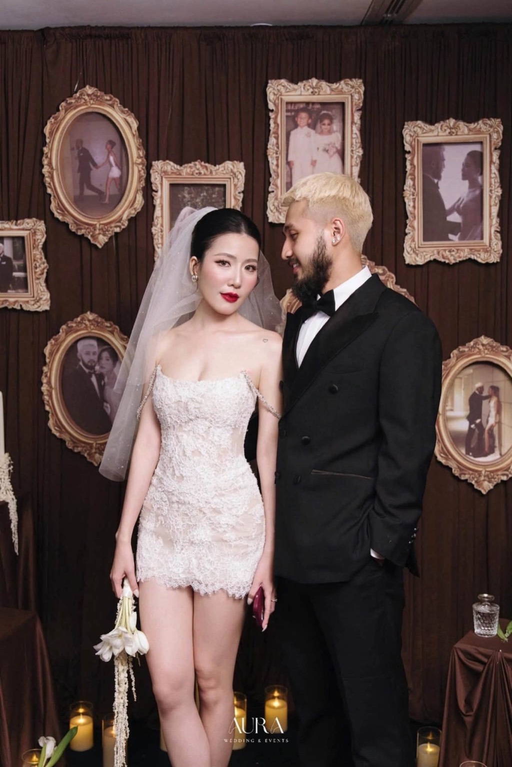 Cô dâu chú rể trước tường khung ảnh vintage mạ vàng trên rèm nâu, nến dưới chân