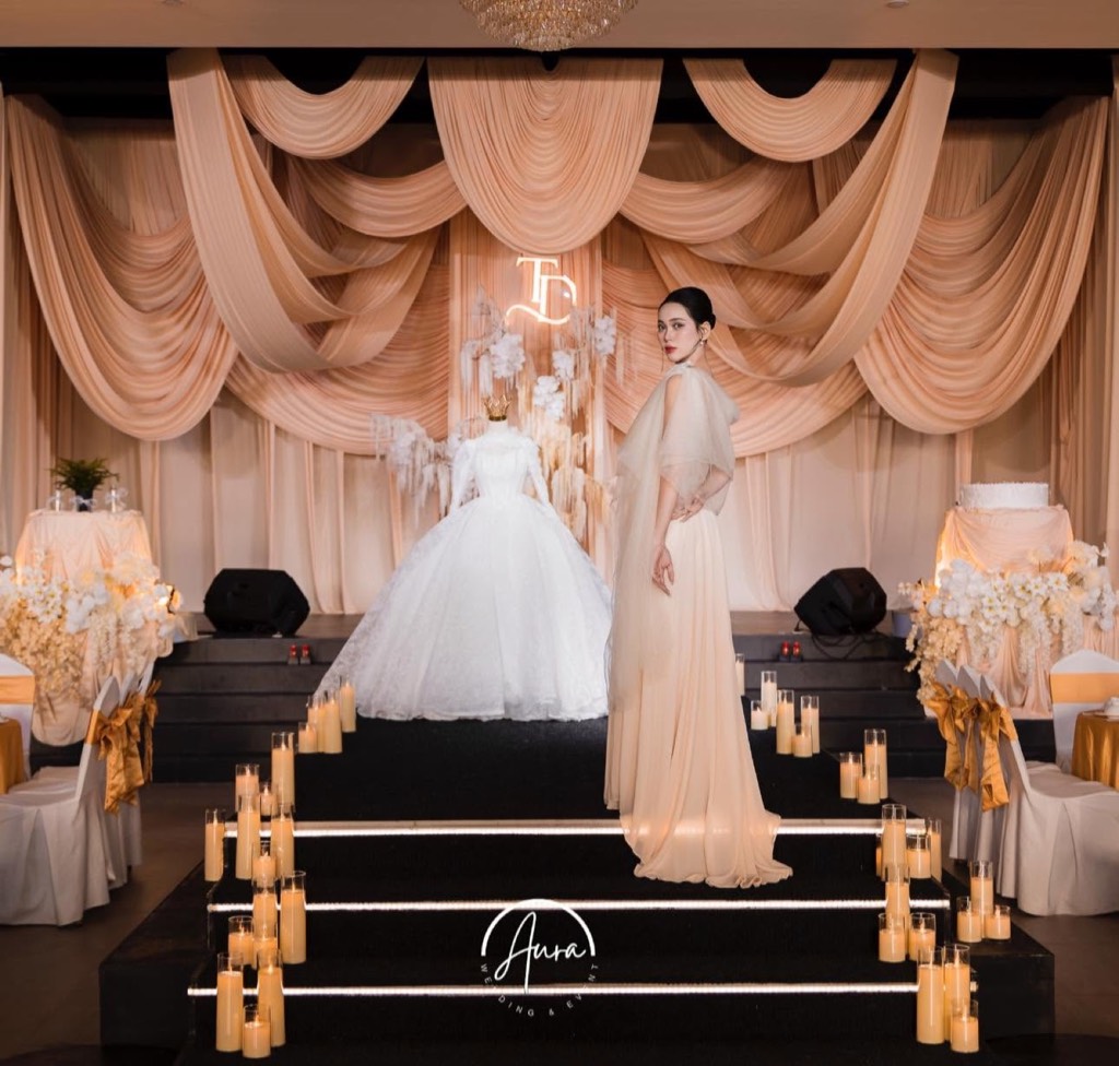 Sân khấu rèm champagne – nude với monogram neon TD, váy cưới trên ma-nơ-canh và bậc thang viền nến