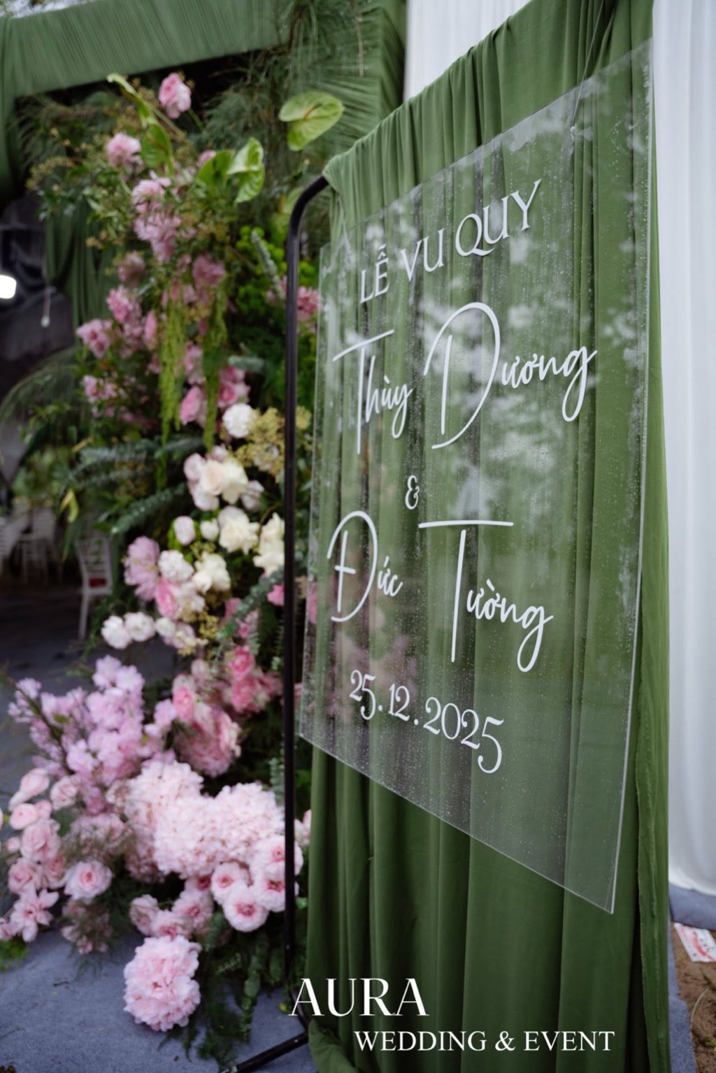 Bảng tên mica trong suốt trên rèm xanh rêu, bên trụ hoa hồng và cẩm tú cầu hồng phấn